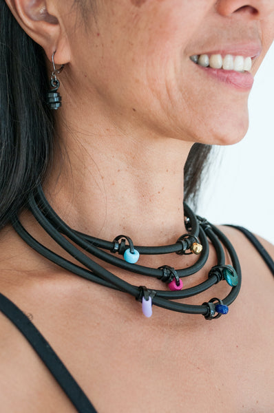 Arvi is wearing 170cm Loopt necklace/bracelet in heavy cord with thin black wire with mixed coloured beads, worn 4x around her neck. She is also wearing matching Loopt earrings in thin black.