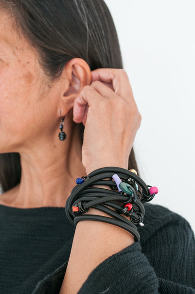 Arvie is wearing a 170cm Loopt in heavy cord with thin black wire with mixed coloured beads as a bracelet. She is also wearing thin black Loopt earrings.