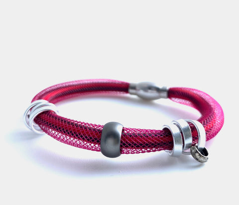 This Bracelet has netted tubing with shock cord, aluminum wire and a coloured bead with a magnetic clasp. It is 21cm.