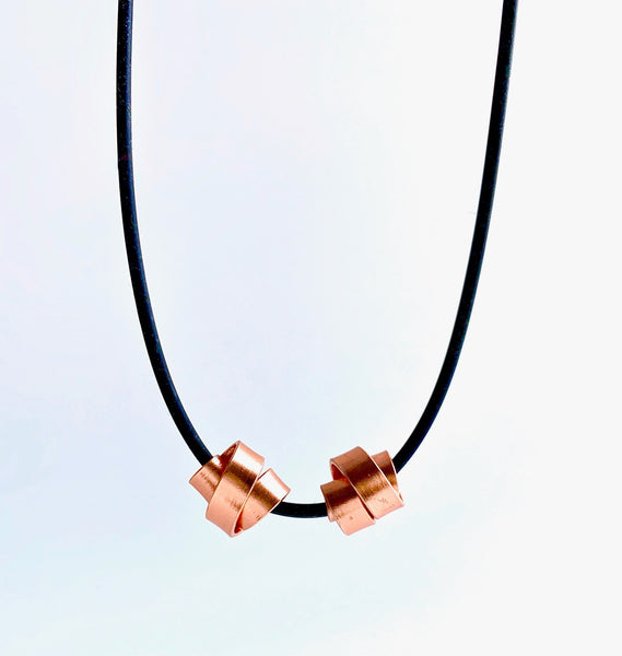 This Rubber Loopt necklace is made of aluminum wire in copper colour. Thes 2 wire pieces can be moved together or apart. It hangs on a rubber necklace with an interlocking clasp.