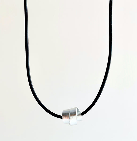 This Rubber Loopt necklace is in flat silver aluminum wire. It hangs on a rubber necklace with an interlocking closure. This piece comes in many variations.