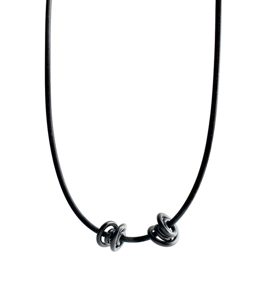 This Rubber Loopt necklace is in round black. Made of aluminum wire and hangs on a rubber necklace with an interlocking closure. This piece comes in many variations.