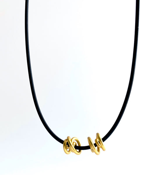 This Rubber Loopt necklace is in round gold. Made of aluminum wire and hangs on a rubber necklace with an interlocking closure. This piece comes in many variations.