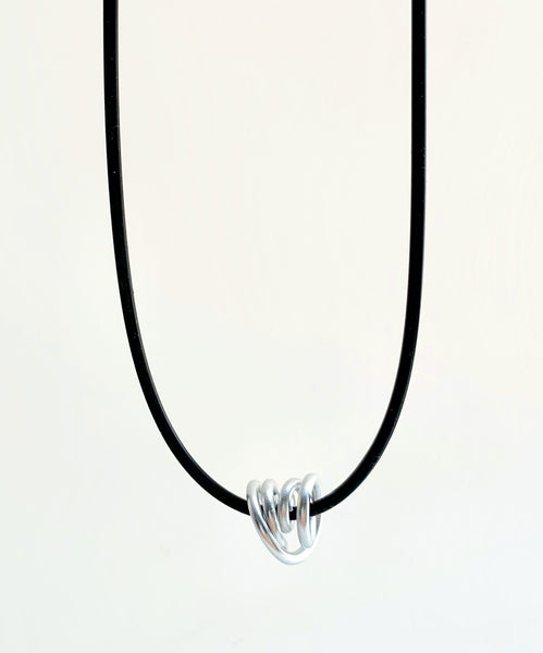 This Rubber Loopt necklace is in round silver. Made of aluminum wire and hangs on a rubber necklace with an interlocking closure. This piece comes in many variations.