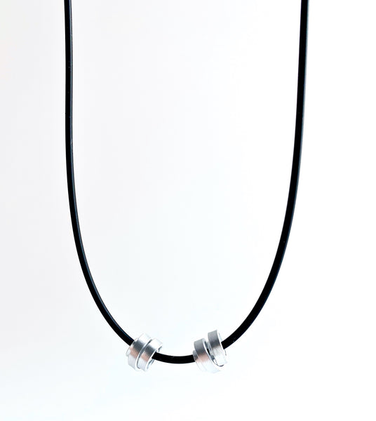 This Rubber Loopt necklace is in thin silver. Made of aluminum wire and hangs on a rubber necklace with an interlocking closure. This piece comes in many variations.